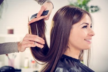 Vrouw met donkerbruin haar laat haar haar knippen door een kapster