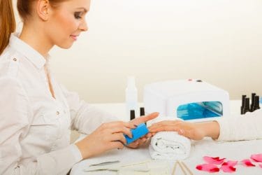 Nagelstyliste brengt gelnagels aan bij een klant.